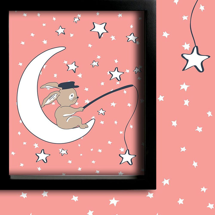 Framed children’s illustration of a rabbit sitting on a crescent moon and fishing for stars against a pink starry background, creating a dreamy and whimsical nursery décor piece