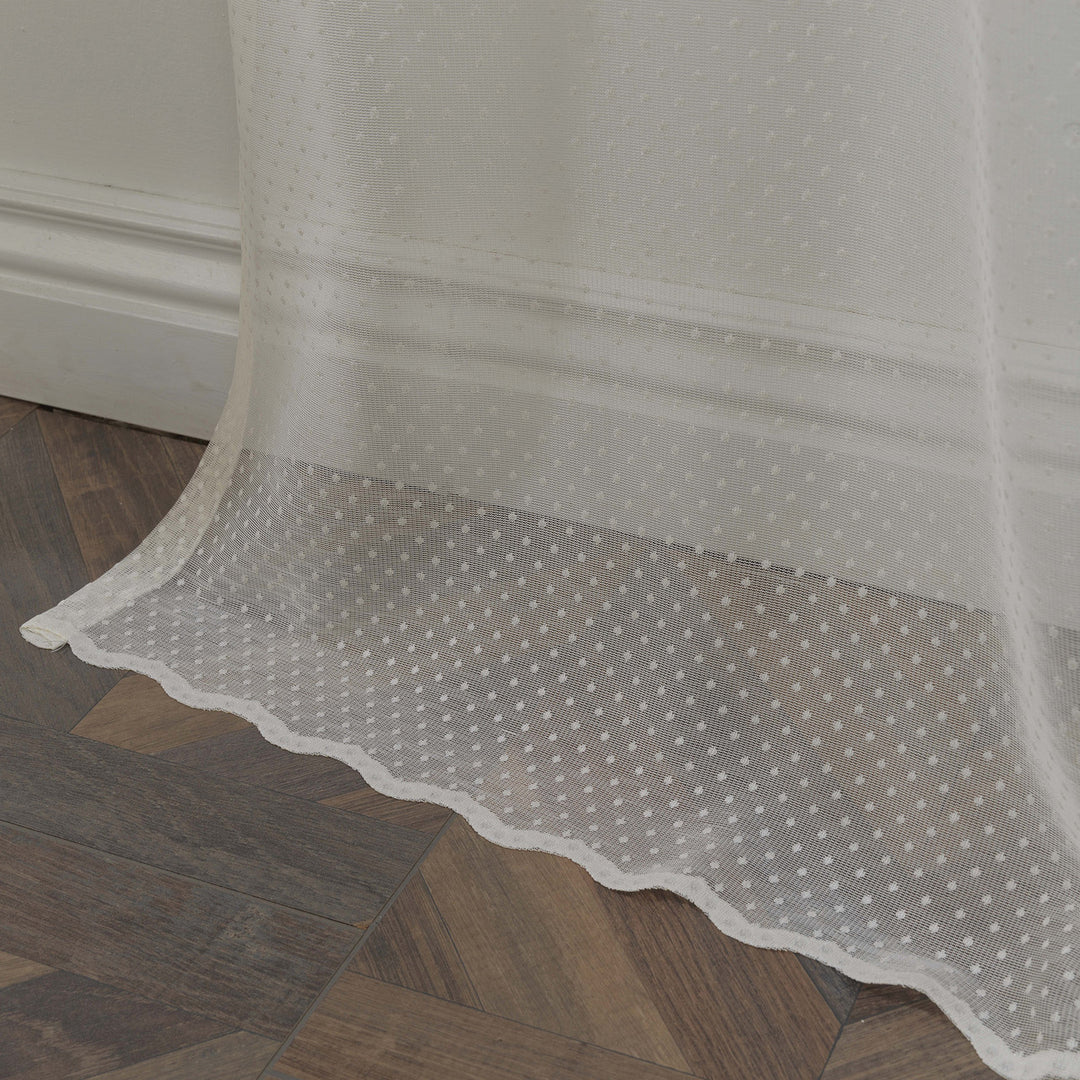 A detailed view of beige polka‑dot sheer voile fabric showing its lightweight airy weave and evenly spaced printed dot pattern