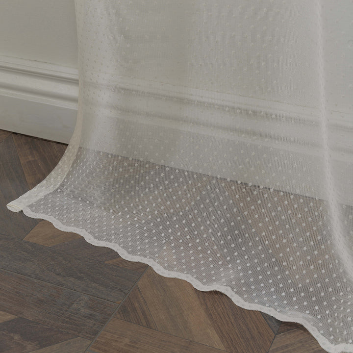 A detailed view of beige polka‑dot sheer voile fabric showing its lightweight airy weave and evenly spaced printed dot pattern