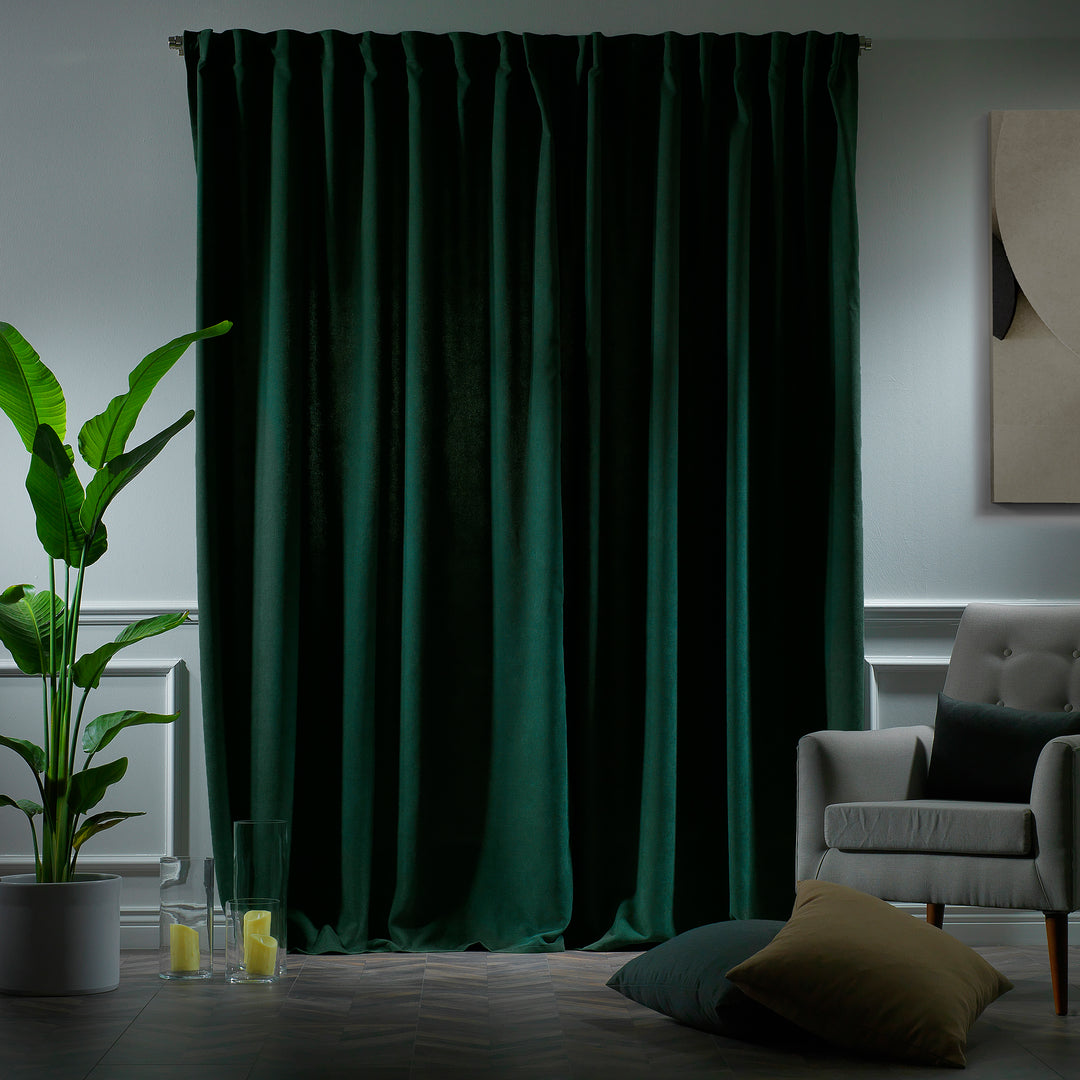 Dark green velour curtains photographed at night, showing deep colour and dense velour texture.