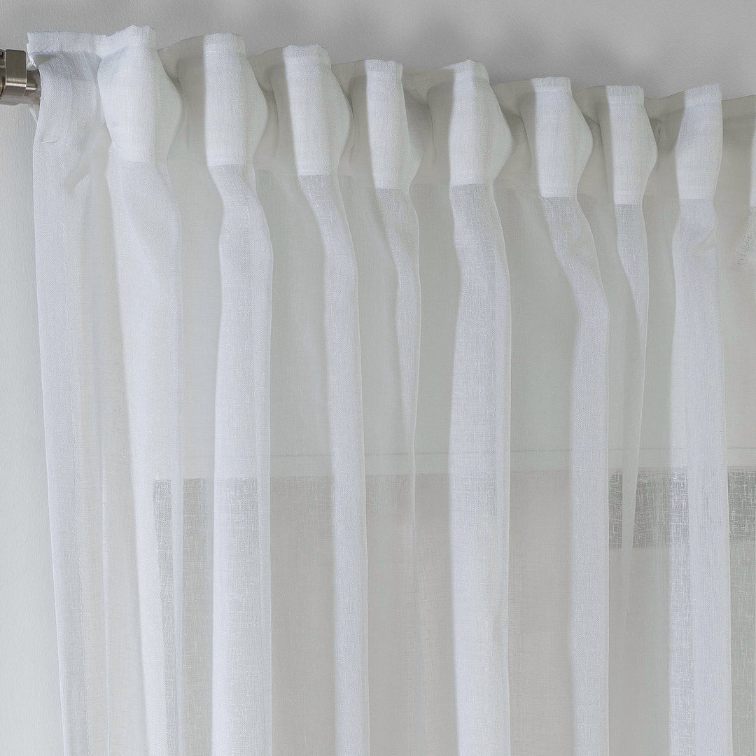 Ecru linen sheer curtain hanging in a cosy bedroom, warm airy drape with soft folds.