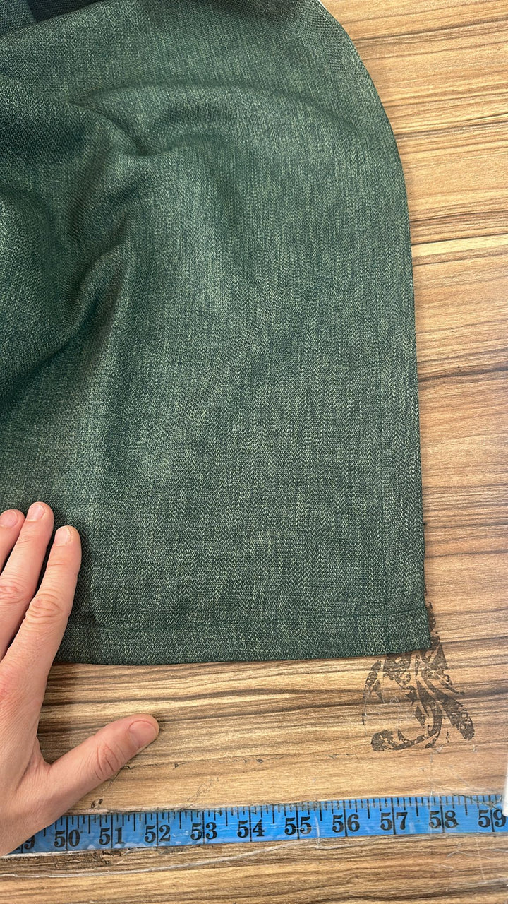 Green fabric on a wooden surface with a hand and ruler for scale