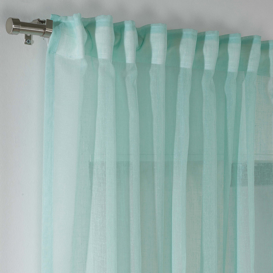Blue green linen sheer curtain hanging in a modern bedroom, cool airy drape with soft folds.